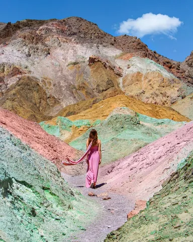 Woman in pink dress walking on colorful mountain path.