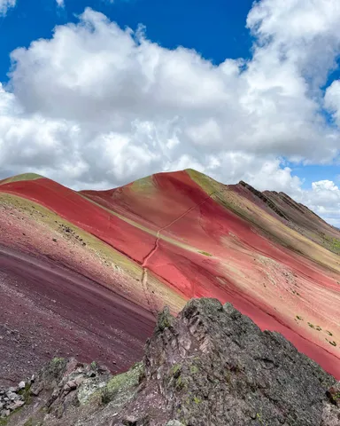 Vibrant red and purple mountain slopes under a cloudy sky.