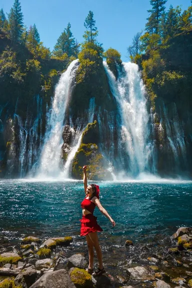 Mujer disfrutando frente a una cascada en un día soleado.